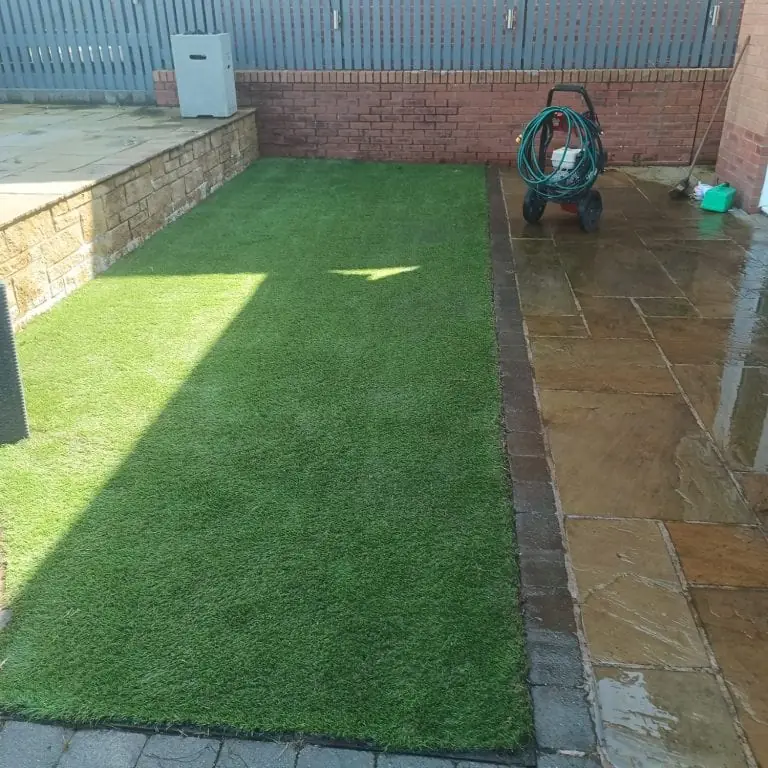 The same artificial lawn after restoration, clean green edges beside the washed patio