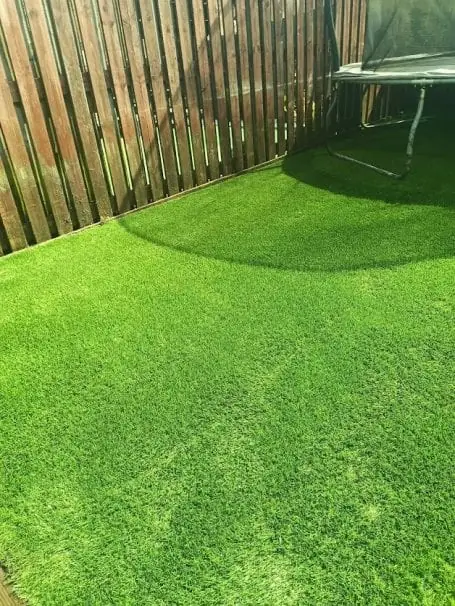 The same garden's artificial grass restored to an even green along the fence line