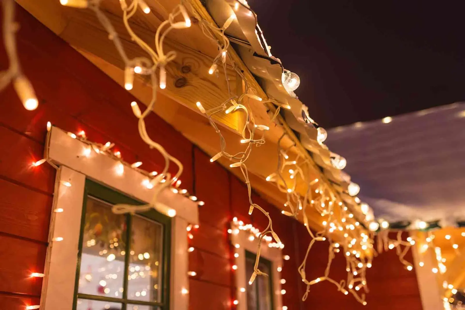 Warm white Christmas lights hanging along a roofline and framing the windows of a house