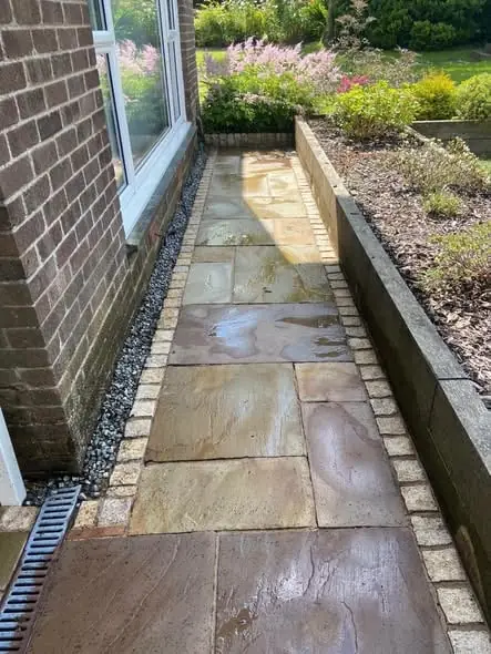 Freshly washed Indian sandstone path running alongside a brick house